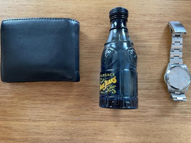 Versace blue jeans bottle next to wallet and rolex for scale